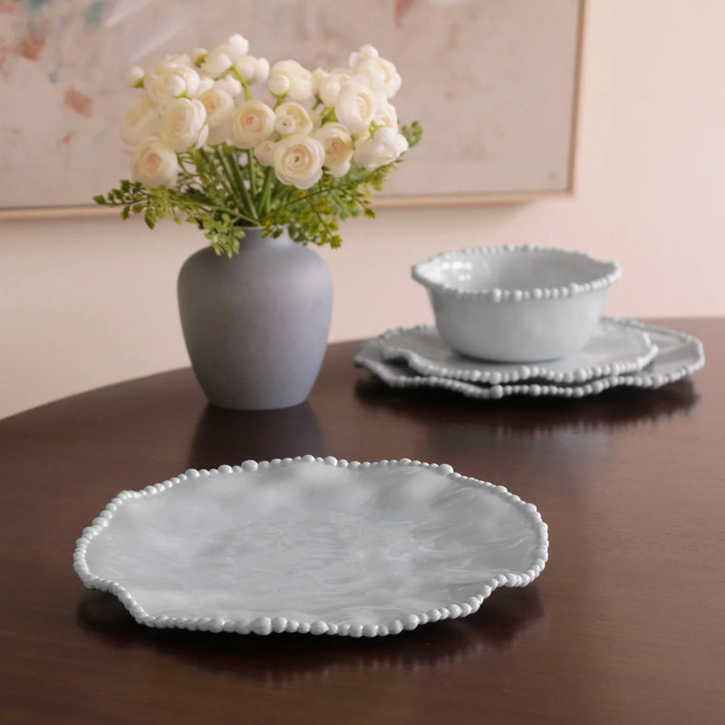 Set of light blue ceramic dishes on a wooden table with a vase of white flowers.