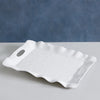 White ceramic tray with wavy edges on a gray surface with a blue background