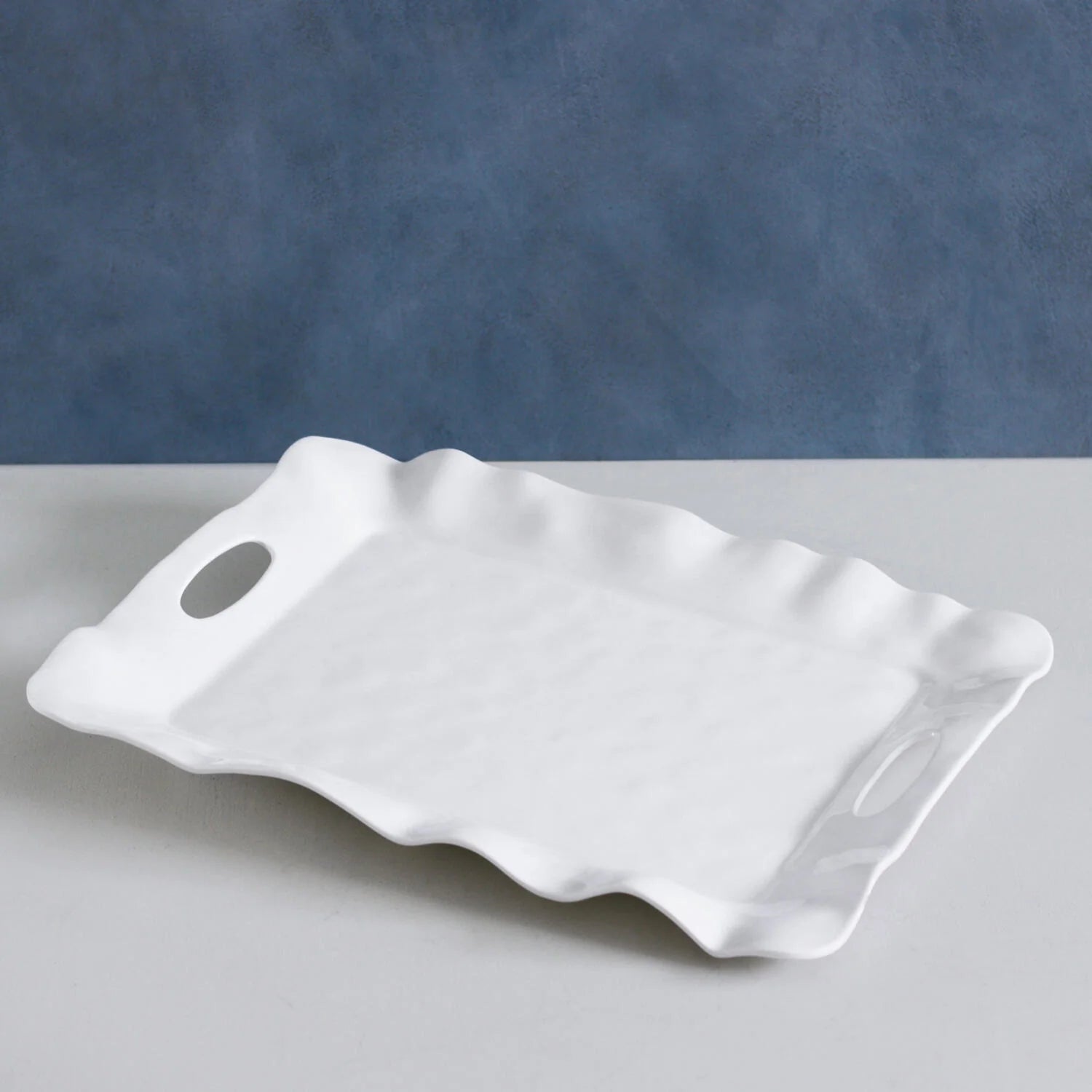 White ceramic tray with wavy edges on a gray surface with a blue background