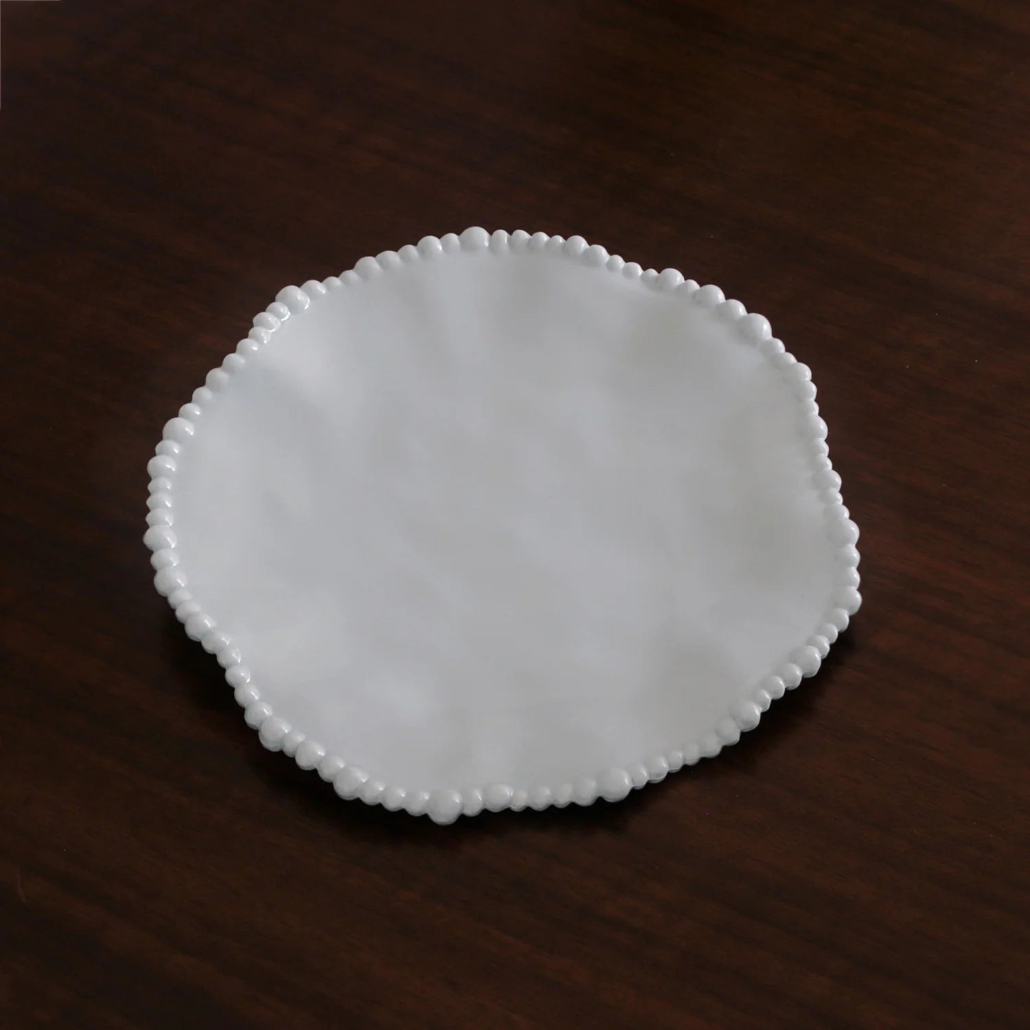 White ceramic plate with decorative edge on a dark wooden surface