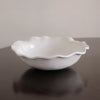White ceramic bowl with wavy edge on a reflective surface