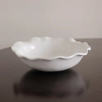 White ceramic bowl with wavy edge on a reflective surface