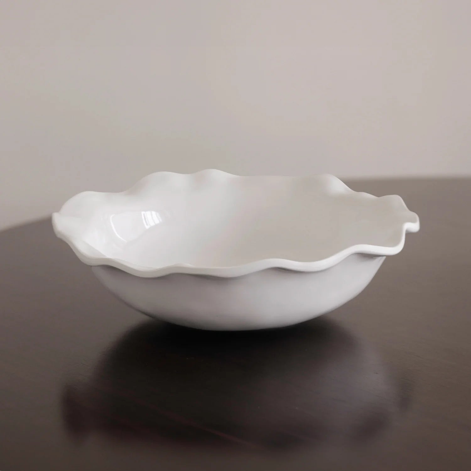 White ceramic bowl with wavy edge on a reflective surface