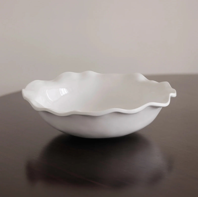 White ceramic bowl with wavy edge on a reflective surface
