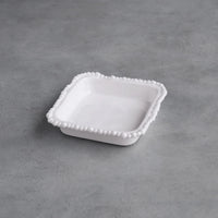 White ceramic dish with decorative edge on a gray concrete surface