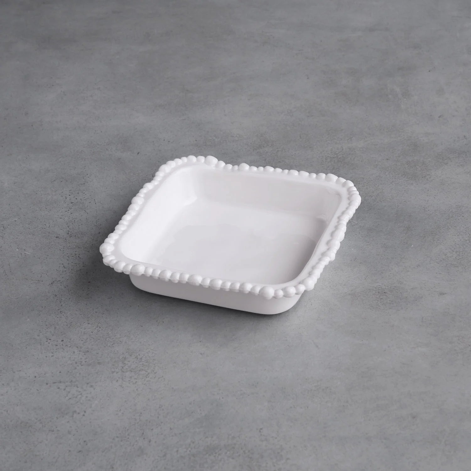 White ceramic dish with decorative edge on a gray concrete surface