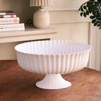 White decorative bowl on a wooden surface with books and a lamp in the background