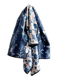 Two floral-patterned towels, one blue and one beige with white patterns, draped over each other on a white background.