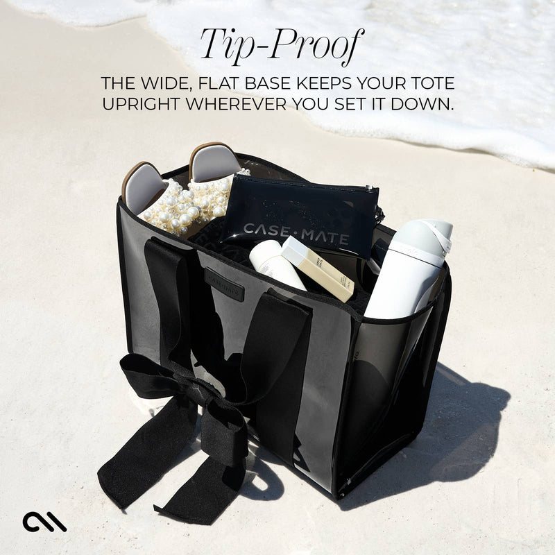 Black tote bag with items on a sandy beach, featuring text about its tip-proof design.