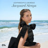 Woman in a black dress with large black bows sitting on a beach, text 'Lightweight & Luxurious Jacquard Straps' above.