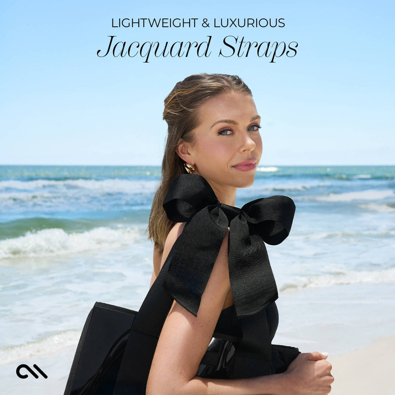 Woman in a black dress with large black bows sitting on a beach, text 'Lightweight & Luxurious Jacquard Straps' above.