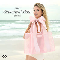Woman holding a pink tote bag with a large bow on a beach