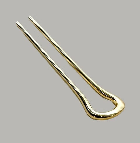 A polished gold metal hair pin, also known as a hair claw clip, shown on a solid gray background.
