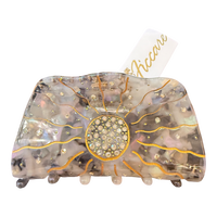 A large hair claw clip by Accare, featuring a translucent iridescent resin body with gold glitter sunburst lines, a central round rhinestone cluster, and small rhinestone accents, shown on a white background with a white paper tag.