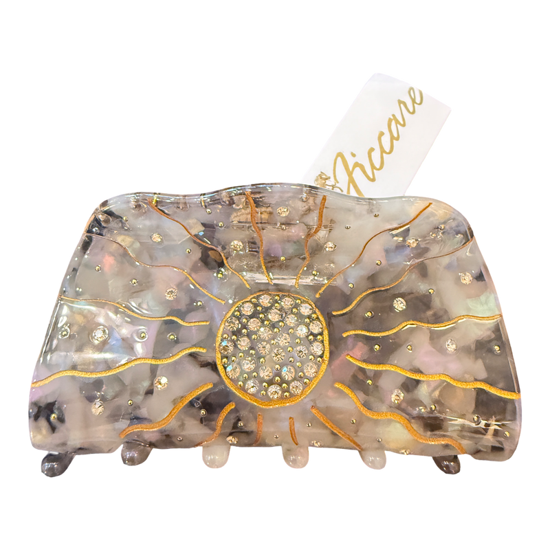 A large hair claw clip by Accare, featuring a translucent iridescent resin body with gold glitter sunburst lines, a central round rhinestone cluster, and small rhinestone accents, shown on a white background with a white paper tag.