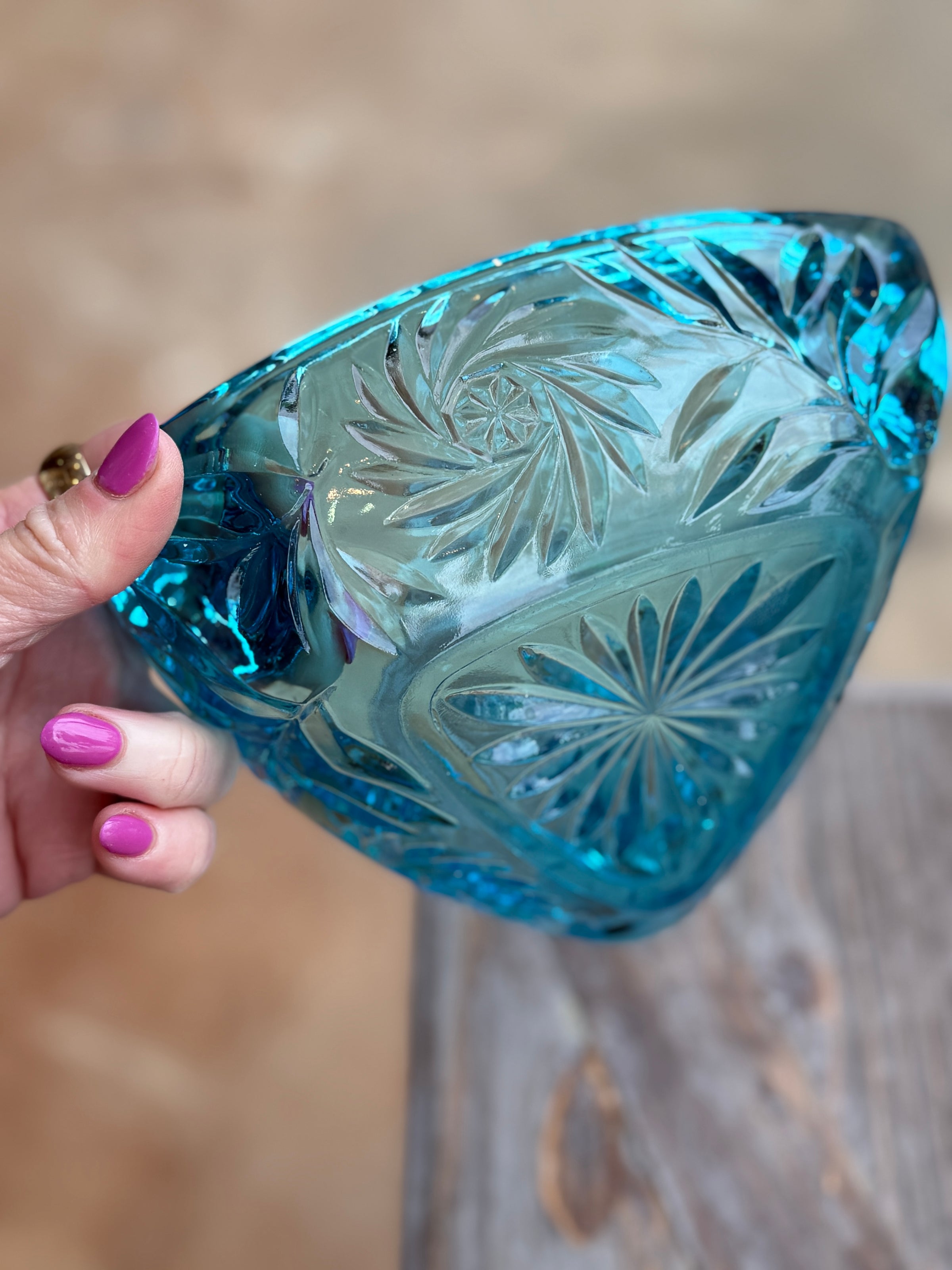 Hand holding a blue glass bowl with intricate patterns against a blurred background