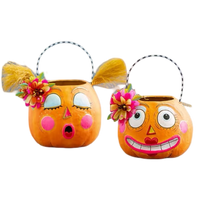 Two orange pumpkin-shaped bucket baskets with decorative faces and floral accents, shown on a plain white background. One has a surprised expression with closed eyes, and the other has a wide smiling expression with open eyes.