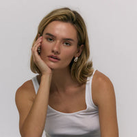 Woman wearing a white tank top against a plain background