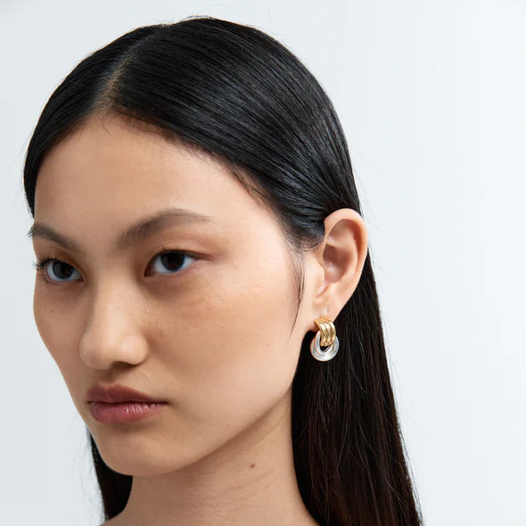 Close-up of a person wearing gold hoop earrings with a plain background