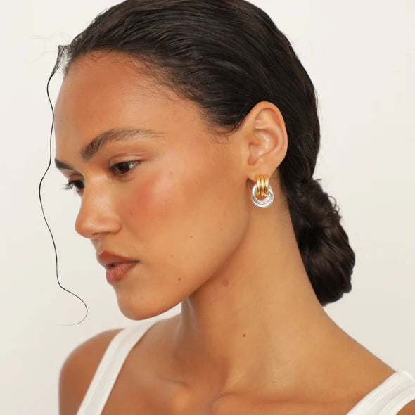 Close-up of a woman wearing gold hoop earrings on a plain background