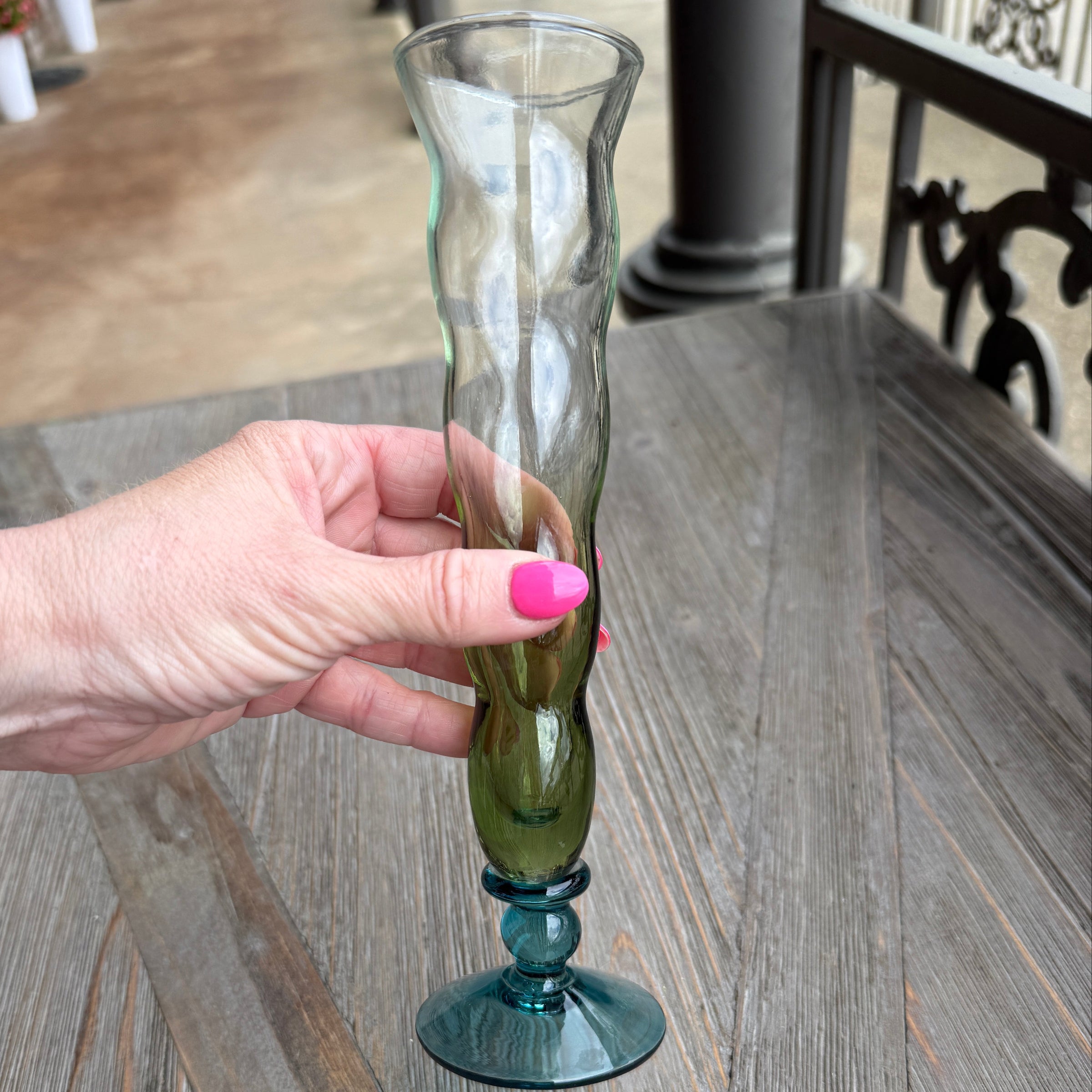 Hand holding a glass bottle with a unique design against a wooden background
