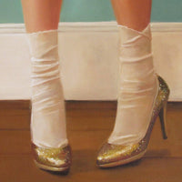 Gold high-heeled shoes with white ribbons on a wooden floor.