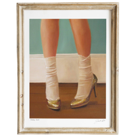 Framed artwork of legs wearing white stockings and gold high heels on a wooden floor.