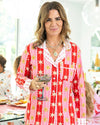 Woman in a red and pink patterned shirt holding a glass of wine in a social setting.