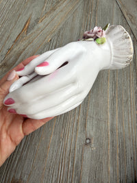 White ceramic glove with pink flowers held by a hand on a wooden surface