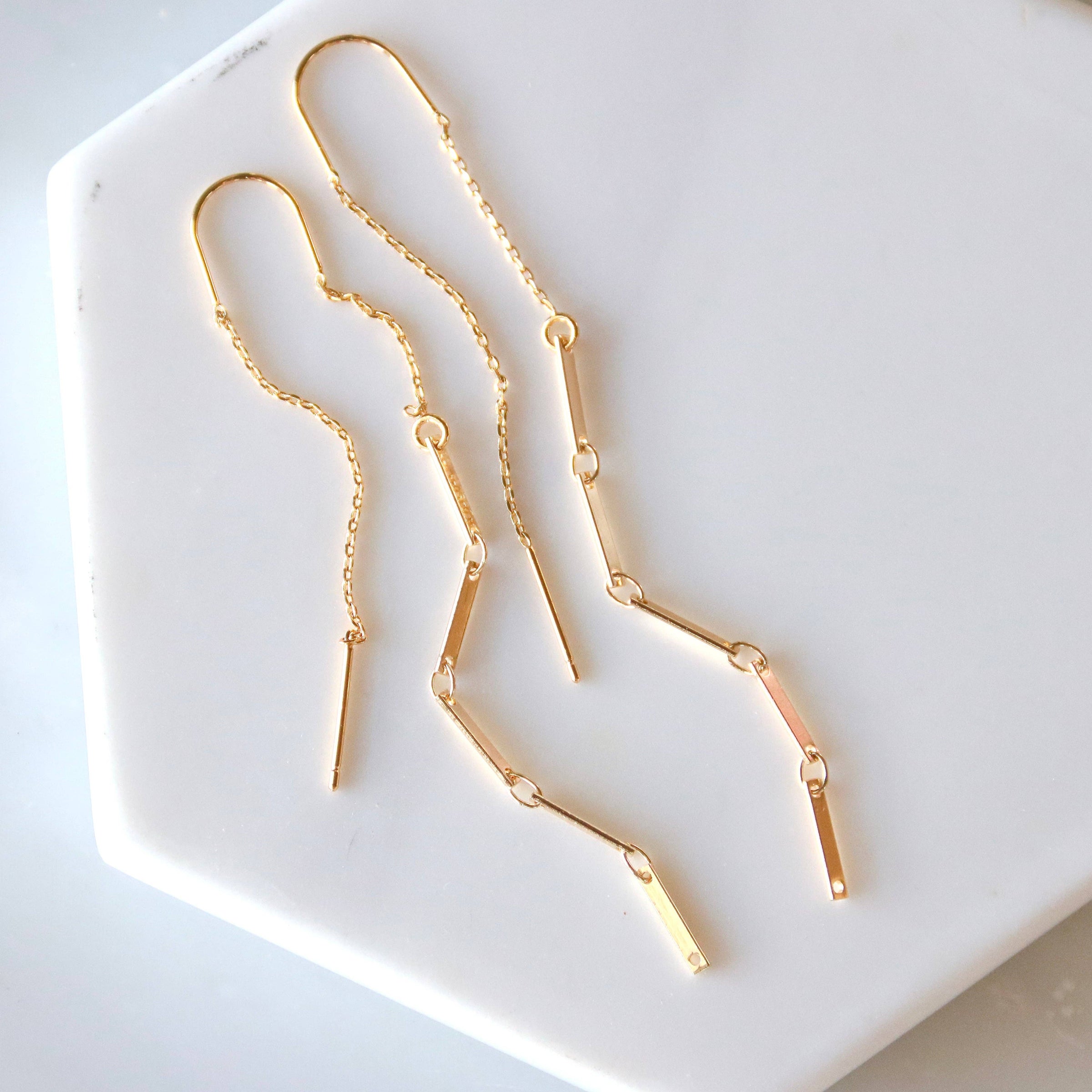 Gold chain earrings on a white hexagonal plate