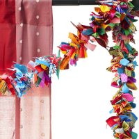 A close-up of a colorful decorative garland made of many layered fabric strips in bright shades, draped along the top and right side of a frame next to a pink fabric panel.
