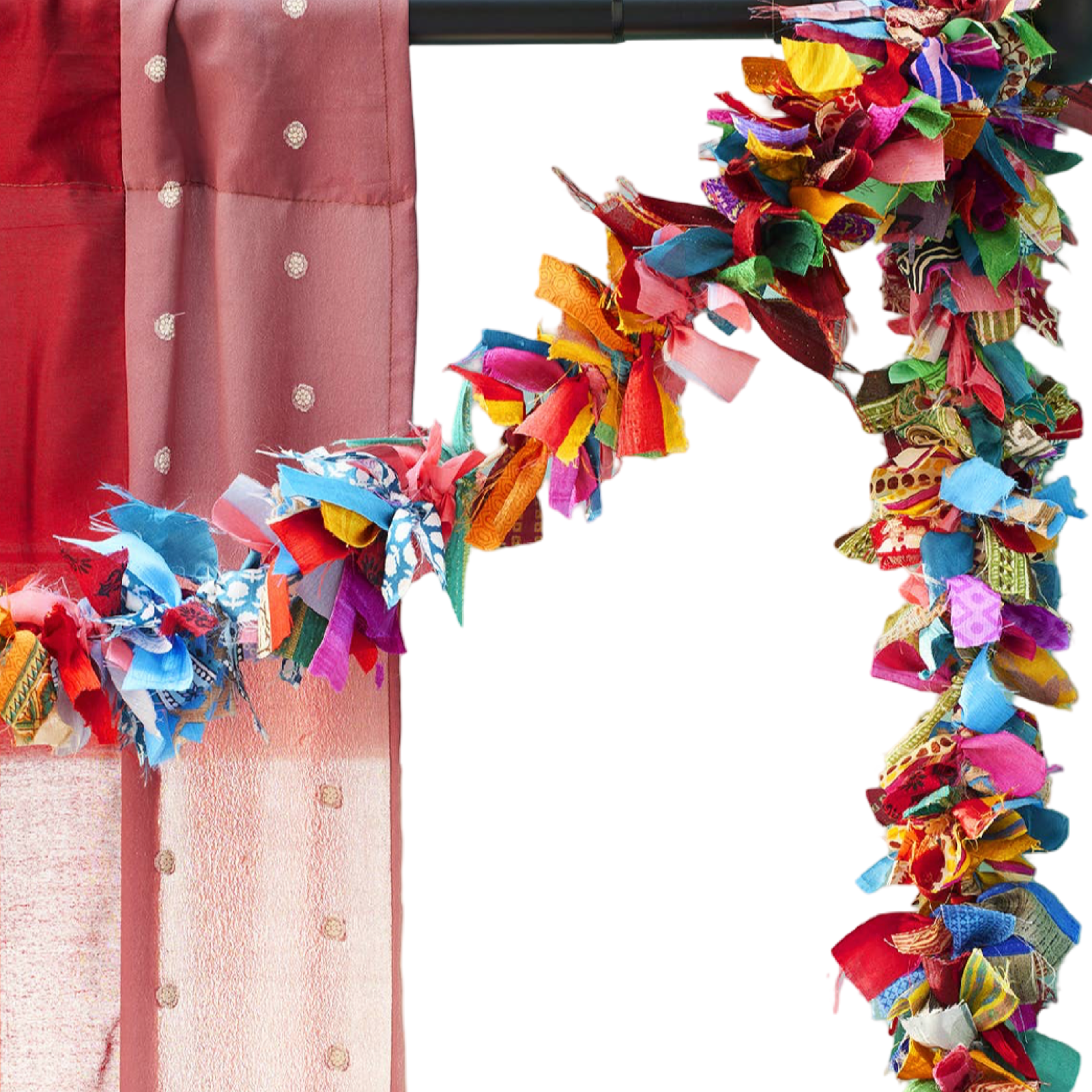 A close-up of a colorful decorative garland made of many layered fabric strips in bright shades, draped along the top and right side of a frame next to a pink fabric panel.