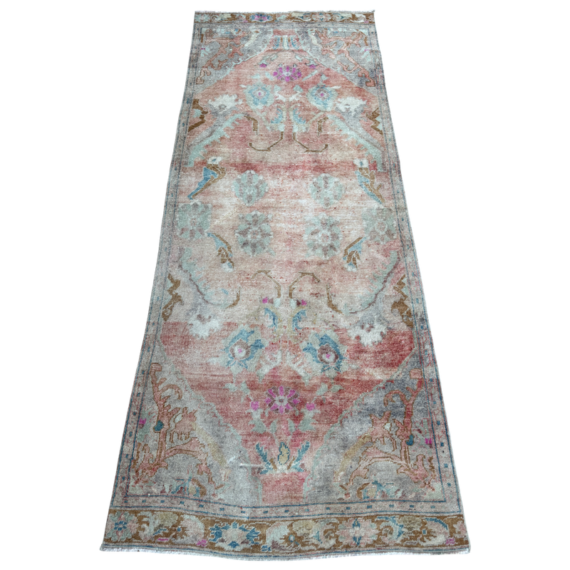 A long rectangular vintage-style area rug with a distressed, faded floral pattern in muted pink, blue, beige, and gray tones, shown flat against a white background.
