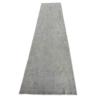 A long rectangular area rug in a distressed light gray color with subtle faded blue-gray and beige undertones, featuring a distressed traditional pattern and short fringe on the ends.