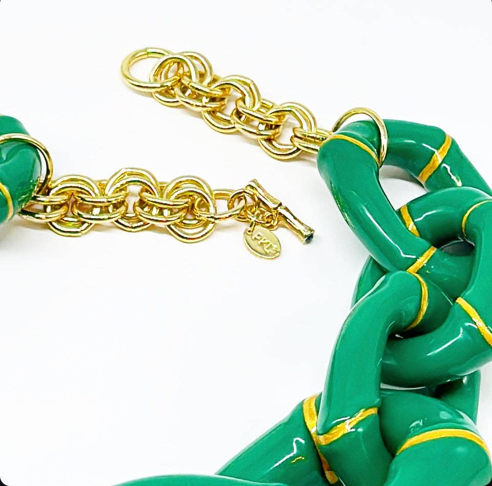 Gold chain bracelet with green links on a white background