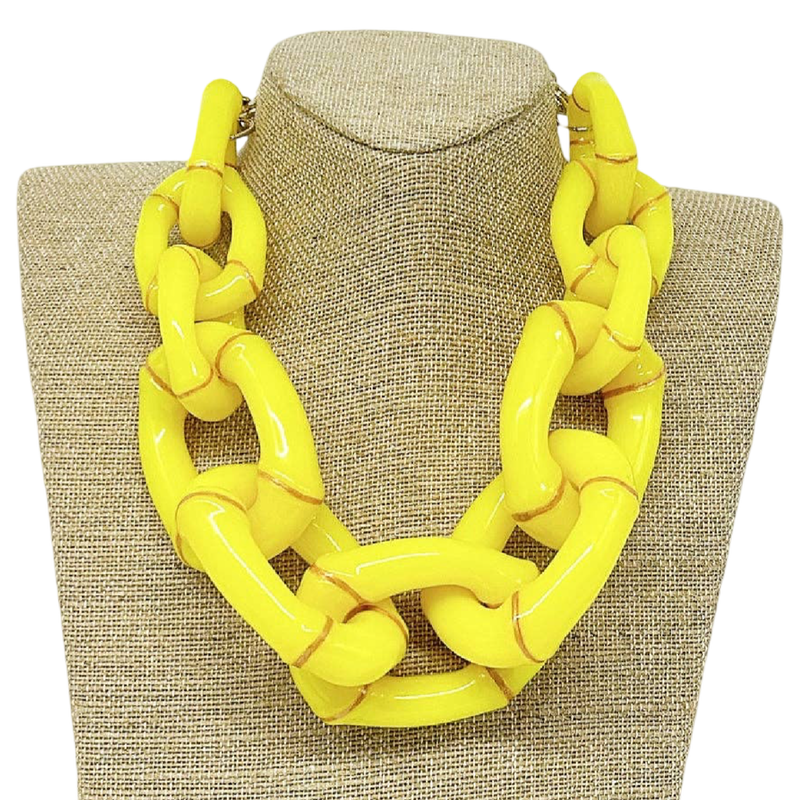 Yellow chain necklace on a textured beige stand