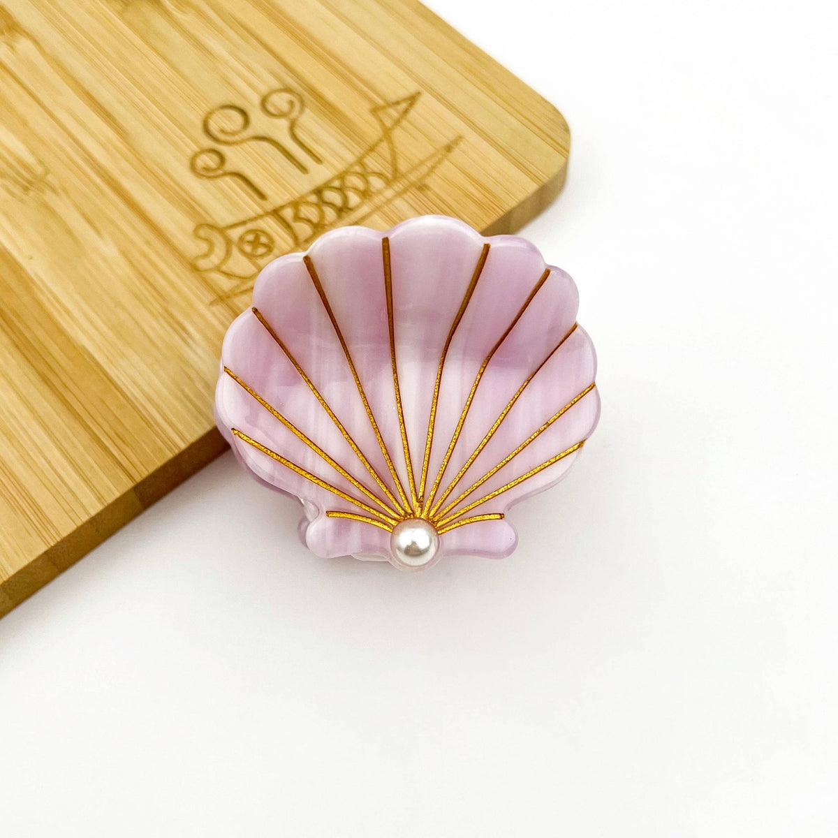 Pink shell-shaped object with gold accents and a pearl on a wooden surface