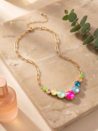 Necklace with colorful beads on a marble surface with a bottle and leaves.