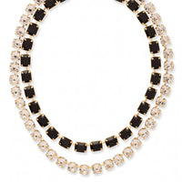 A gold-toned tennis necklace featuring two rows of stones: one row with square black gemstones and the other with round clear gemstones, set against a plain white background.