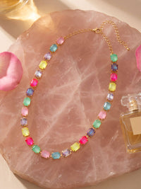 Colorful beaded necklace on a pink stone surface with a perfume bottle.