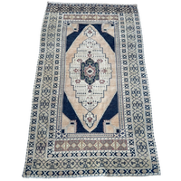 Vintage Turkish hand-knotted rug measuring approximately 3 feet 8 inches by 6 feet 4 inches with deep navy blue, cream, faded blush and green geometric medallion pattern.