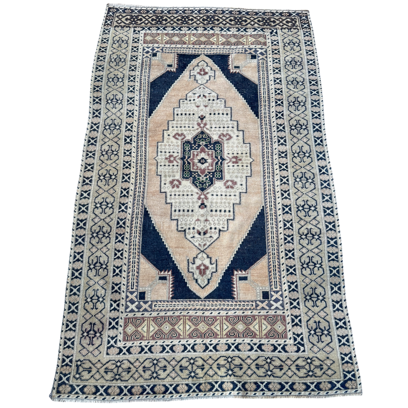 Vintage Turkish hand-knotted rug measuring approximately 3 feet 8 inches by 6 feet 4 inches with deep navy blue, cream, faded blush and green geometric medallion pattern.