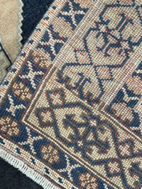 Close-up of a woven rug corner showing a cream and navy geometric pattern with brown accents and white fringe.
