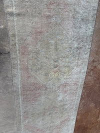 A close-up of a distressed area rug with a faded traditional pattern in muted tones of gray, beige, and dusty pink, laid flat on a concrete floor.