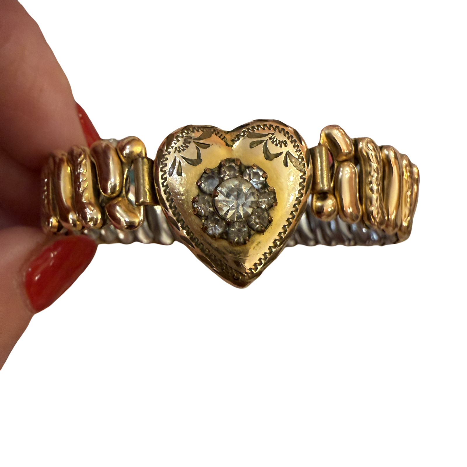 A gold heart-shaped cuff bracelet with a central diamond cluster, held by a hand with red nail polish against a white background.