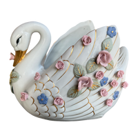 A decorative ceramic swan figurine with a glossy white body, gold-painted lines, and raised pink, blue, and green floral details, shown on a plain white background.
