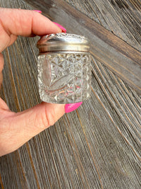 Hand holding a decorative glass container with a silver base on a wooden surface