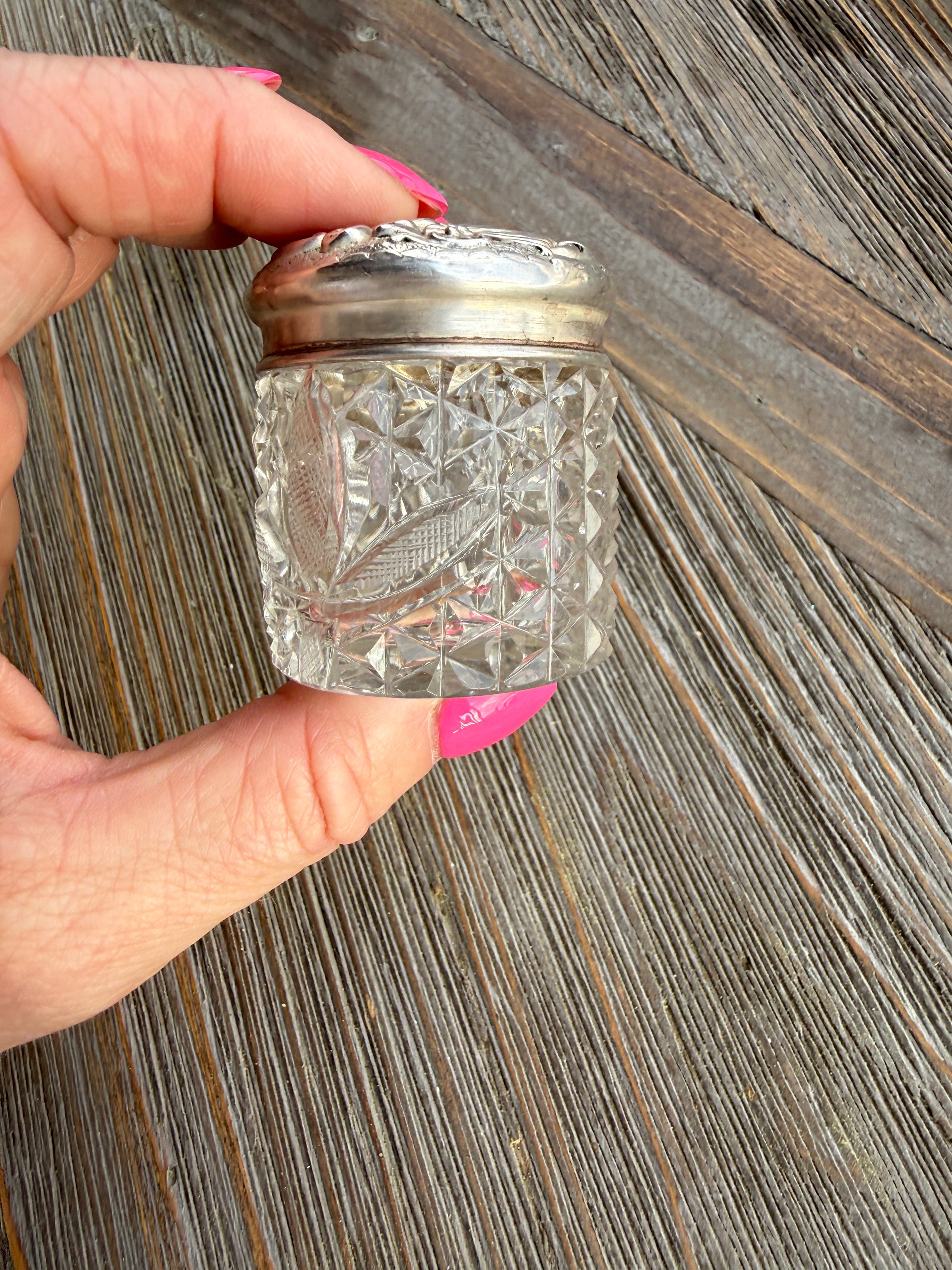 Hand holding a decorative glass container with a silver base on a wooden surface