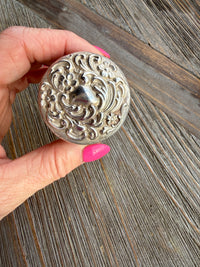 Hand holding a decorative silver button against a wooden background