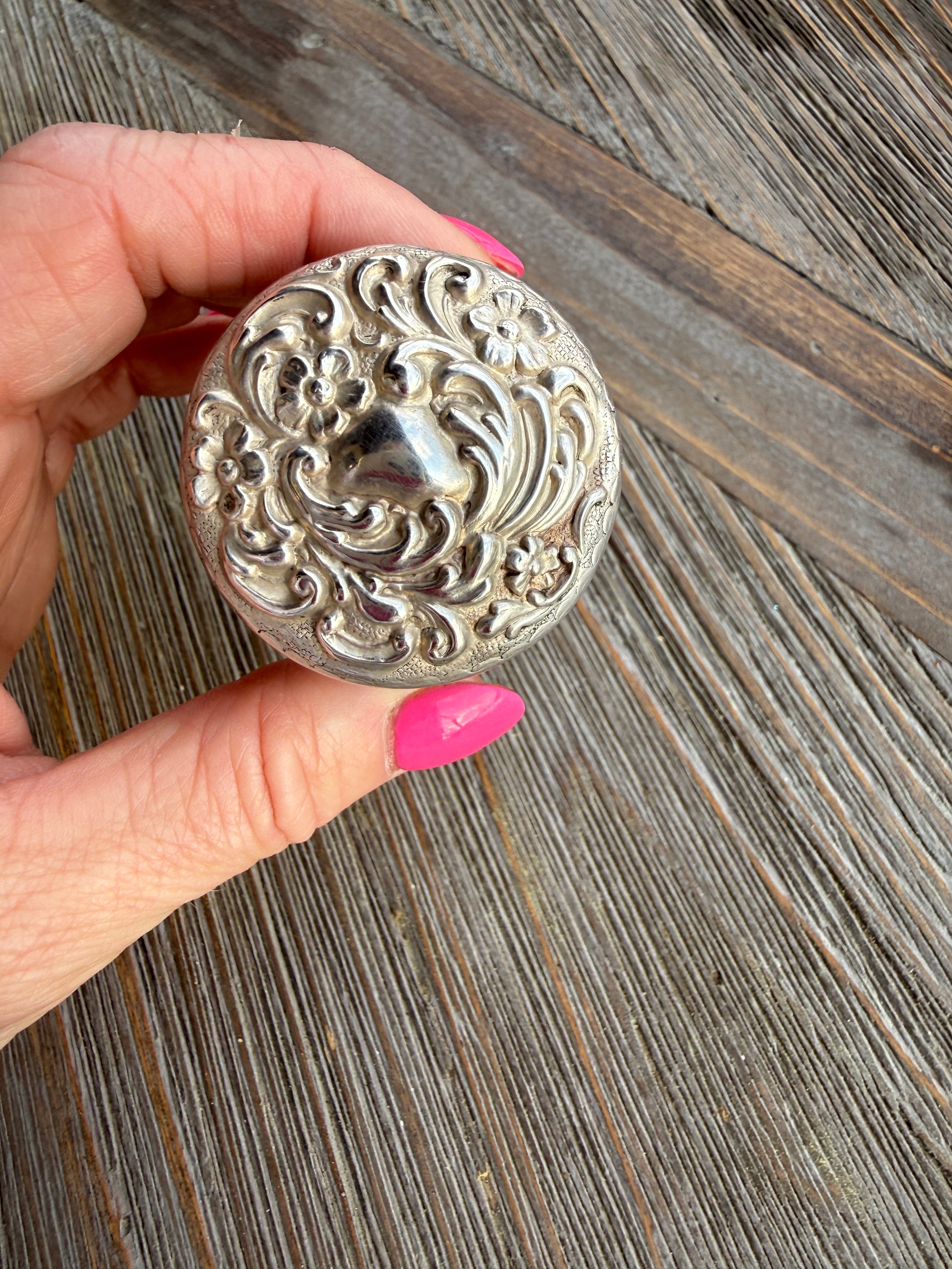 Hand holding a decorative silver button against a wooden background